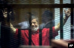 Former Egyptian President Mohamed Morsi, wearing a red jumpsuit that designates he has been sentenced to death, raises his hands inside a defendants cage in a makeshift courtroom at the national police academy, in an eastern suburb of Cairo, June 18, 2016.