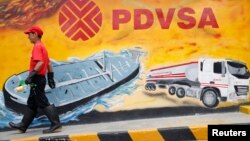 Un trabajador camina frente a un mural con el logo de PDVSA, en una estación en Caracas.