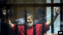 L'ancien président égyptien Mohamed Morsi, condamné à mort et vêtu d'une combinaison rouge, lève ses mains à l'intérieur de la cage des accusés, lors d’une audience à l'académie de police nationale, dans une banlieue est du Caire, en Egypte, 18 juin 2016. 