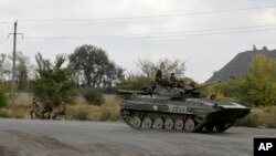 Pro-Russian gunmen sits atop armored personal carrier as they pass through the checkpoint near the town of Zhdanivka, eastern Ukraine, Sept. 23, 2014.