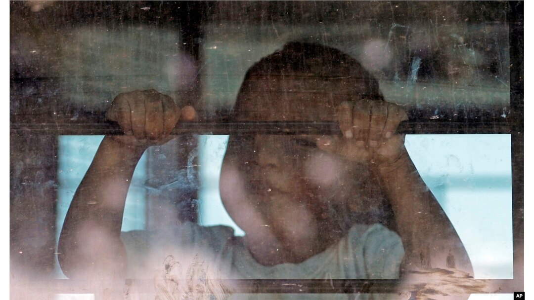 Un niño inmigrante mira desde un autobús de la Patrulla Fronteriza de EE.UU. mientras los manifestantes bloquean la calle frente al Centro de Procesamiento Central de la Patrulla Fronteriza de los Estados Unidos el sábado 23 de junio de 2018 en McAllen, Texas.
