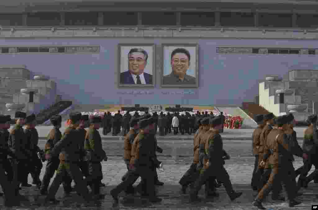 North Korean soldiers march on Kim Il Sung Square in Pyongyang as others pay their respects beneath portraits of the late leaders Kim Jong Il, right, and Kim Il Sung, Dec. 17, 2013. 