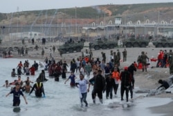 Warga Maroko berjalan di pantai saat petugas Spanyol berpatroli di daerah dekat pagar perbatasan, di pantai El Tarajal, setelah ribuan orang berenang melintasi perbatasan Spanyol-Maroko di Ceuta, Spanyol, 18 Mei 2021. REUTERS / Jon Nazca