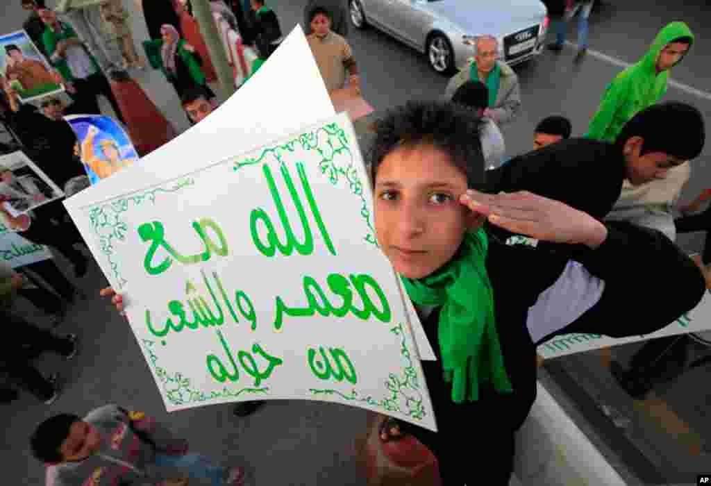 A Gadhafi supporter holds a sign outside Bab Al-Aziziyah, Gadhafi's heavily fortified Tripoli compound, March 19, 2011. The sign reads, "God is with Muammar and people around him". (Reuters)