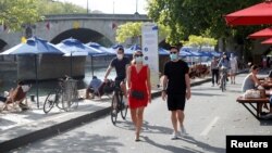 Para pejalan kaki mengenakan masker wajah berjalan di pinggiran Sungai Seine, Perancis, setelah Perancis mewajibkan penggunaan masker di tempat umum untuk mencegah penyakit Covid-19 muncul kembali, Sabtu, 15 Agustus 2020. (Foto: Reuters)