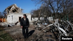 A man walks past a residential building and car damaged by recent shelling in Donetsk, eastern Ukraine, Nov. 6, 2014.