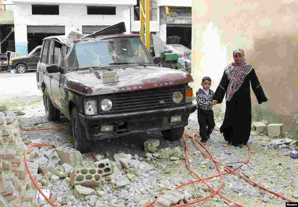 24일 시리아 베카에서 반군의 공격으로 손상된 차량 옆을 지나는 시민들.