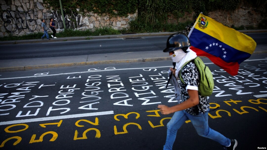 Un manifestante llevando una bandera venezolana corre junto a una lista de las víctimas de la violencia durante protestas contra el gobierno del presidente de Venezuela, Nicolás Maduro en Caracas. Junio 12 de 2017.
