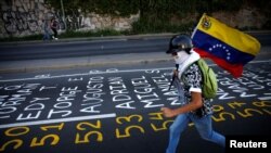 Un manifestante llevando una bandera venezolana corre junto a una lista de las víctimas de la violencia durante protestas contra el gobierno del presidente de Venezuela, Nicolás Maduro en Caracas. Junio 12 de 2017.