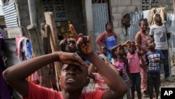 Un niño señala un helicóptero que se acerca y trae ayuda para los sobrevivientes del terremoto en un vecindario cerca del aeropuerto en Les Cayes, Haití, el jueves 19 de agosto de 2021.