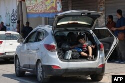 Seorang anak duduk di bagian belakang mobil di tengah kerumunan warga Palestina dengan paspor asing yang menunggu gerbang Rafah dengan harapan bisa menyeberang ke Mesir, Sabtu, 14 Oktober 2023. (Foto: Said Khatib/AFP)