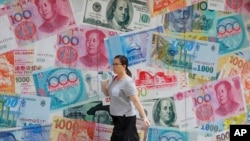 A woman walks by a money exchange shop decorated with different countries currency banknotes at Central, a business district in Hong Kong, Tuesday, Aug. 6, 2019. China's yuan fell further Tuesday against the U.S. dollar, fueling fears about…