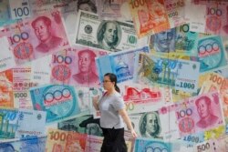 A woman walks by a money exchange shop decorated with different countries currency banknotes at Central, a business district in Hong Kong, Tuesday, Aug. 6, 2019.