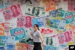 A woman walks by a money exchange shop decorated with different countries currency banknotes at Central, a business district in Hong Kong, Tuesday, Aug. 6, 2019.