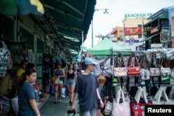FILE - Tourists walk past street vendor shops at the Khao San tourist street in Bangkok, Thailand, Aug. 1, 2018.