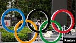 Seorang perempuan yang mengenakan masker pelindung di tengah wabah Covid-19 mengambil gambar logo Olimpiade di depan Stadion Nasional di Tokyo, Jepang, 14 Oktober 2020. (Foto: Reuters)