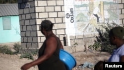 Dua perempuan berjalan melewati sebuah tembok dengan tulisan Oxfam di dindingnya di Port-au-Prince, Haiti (foto: ilustrasi). 
