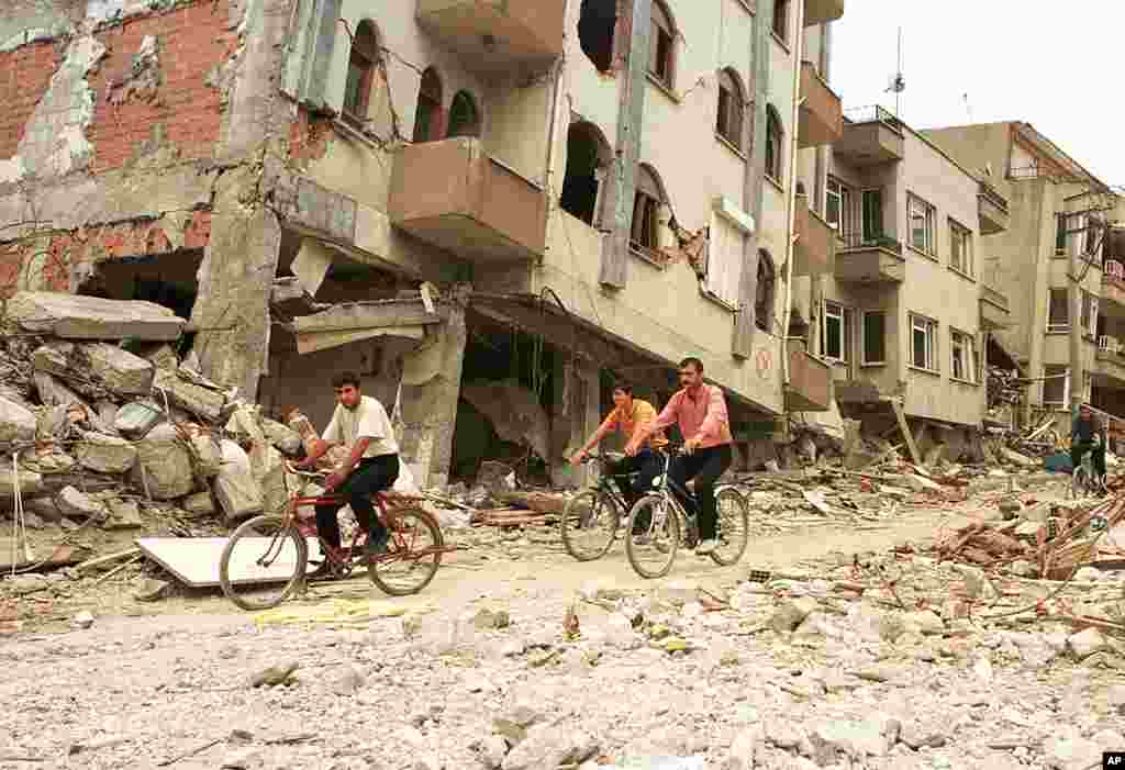 Earthquake survivors with bicycles pass by collapsed buildings in the western Turkish city of Adapazari, September 7, 1999. (AP)