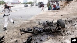 Seorang tentara Somalia lari untuk menembak dekat bangkai mobil yang meledak karena bom selama serangan ke parlemen Somalia (24/5). (AP/Farah Abdi Warsameh)