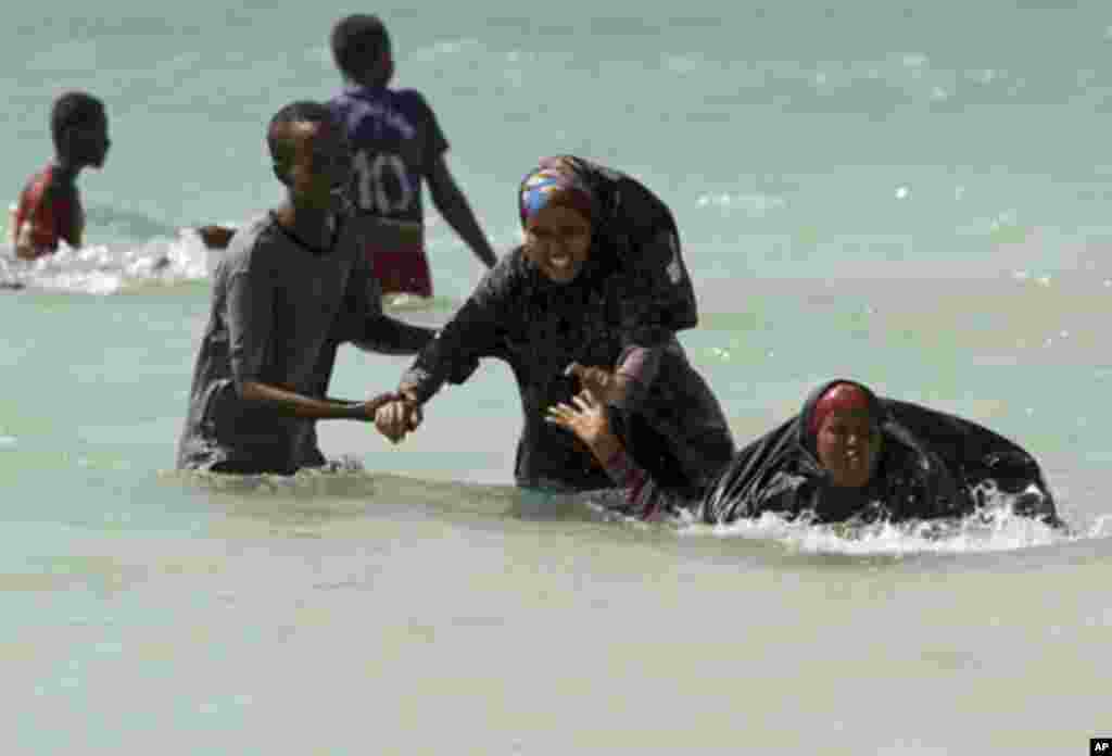 A man guides Somali women near Lido beach in the waters of the Indian Ocean, north of the capital Mogadishu January 6, 2012. Lido beach was a famous attraction before Somalia tumbled into chaos in 1991 with the ousting of dictator Mohamed Siad Barre. In t