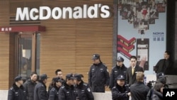 Police officers ask a journalist, lower right, to leave as he covers people gathering in front of a McDonald's restaurant which was a planned protest site in Beijing, February 20, 2011.