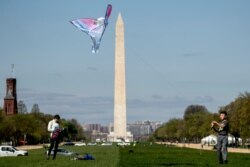 In this April 6, 2020 photo, the Washington Monument is visible behind a boy as he flies a kite on the National Mall in Washington. The warmer weather is bringing increased violations of social distance guidelines in the nation’s capital.