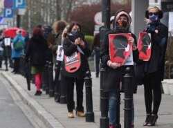 FILE - Women's rights activists, wearing masks to guad  against the spread of the coronavirus, protest against a draft law tightening Poland's strict anti-abortion law near the parliament that was debating it, Warsaw, April 15, 2020.