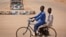 Two boys riding a bicycle pass by campaign posters for opposition candidate Gen. Muhammadu Buhari on a roundabout in Daura, his home town, in Katsina state in northern Nigeria, March 27, 2015. 