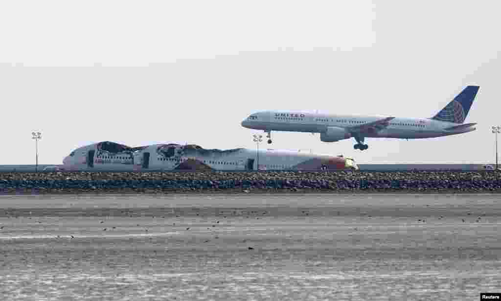 An aircraft lands behind the wreckage of the Asiana Airlines plane at San Francisco International Airport, July 8, 2013. 