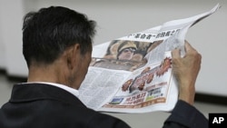 A man reads a local newspaper's story on the spread pages featuring a photo of Moammar Gadhafi at a private securities company in Shanghai, China, Oct. 21, 2011.