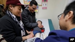 FILE - Matilde Gonzalez, left, and Cesar Calles, hold their son, Cesar Julian Calles, 10 months old, as Ana Martinez, a medical assistant at the Sea Mar Community Health Center, gives him a flu shot in Seattle, Jan. 11, 2018.