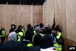 Protesters wearing yellow vests remove wooden boards protecting a shop windows during a demonstration against the rising costs of living that they blame on high taxes in Paris, Dec. 8, 2018.