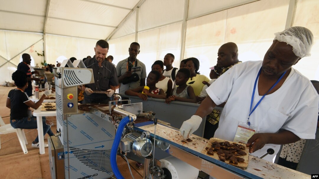 FILE - Visitors watch as employees of a Chocolatier in the Ivory Coast explain and show the different stages of processing cocoa into chocolate during the 5th edition of the ice cream and chocolate festival in Abidjan on May 19, 2018. 