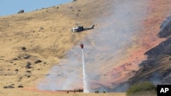 Un helicóptero de la Patrulla de Caminos de California lanza agua para apagar el fuego causado por el accidente de un avión espía de la Fuerza Aérea en misión de entrenamiento.