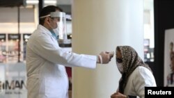 A man checks a woman's temperature, to let her go inside the mall, following the outbreak of the coronavirus disease (COVID-19), after shopping malls and bazaars reopened in Tehran, Iran, April 20, 2020. WANA (West Asia News Agency)/Ali Khara via REUTERS.