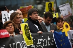 Catalonia's former regional president Carles Puigdemont, center, holds a banner with others during a protest in front of the European Commission headquarters in Brussels, Oct. 15, 2019.
