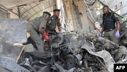 Police anti-bomb officers stand on the burnt engine of the Jeep used by the suicide bomber that ravaged This Day Newspapers.