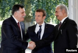 FILE - French President Emmanuel Macron stands between Libyan Prime Minister Fayez al-Sarraj, lefr, and General Khalifa Haftar, commander in the Libyan National Army), who shake hands last year after talks over a political deal to help end Libya's crisis.