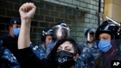 An anti-government protester wearing a mask to help curb the spread of the coronavirus with Arabic that reads, "Revolution," chants slogans while riot police stand guard in front of the Ministry of Economy, in downtown Beirut, Lebanon, May 11, 2020.