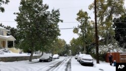 Pedestrians make their way along a snow covered street lined with trees that still have their leaves during a fall snowstorm in Helena, Montana, Sept. 29, 2019.