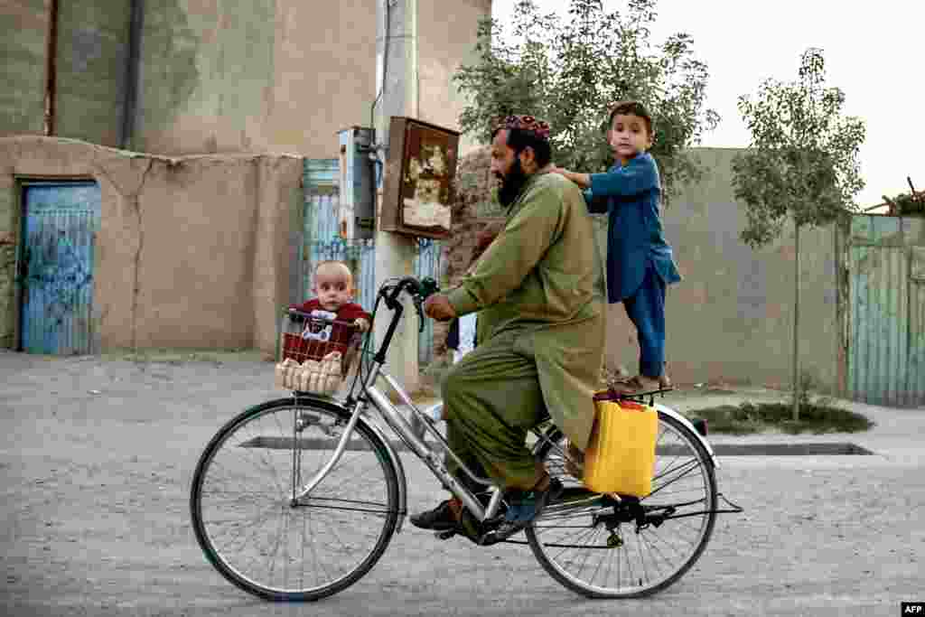 Seorang pria Afghanistan mengendarai sepeda dengan membawa dua anaknya, di sepanjang jalan di desa Rabat di distrik Sholgara, provinsi Balkh. (AFP)&nbsp;