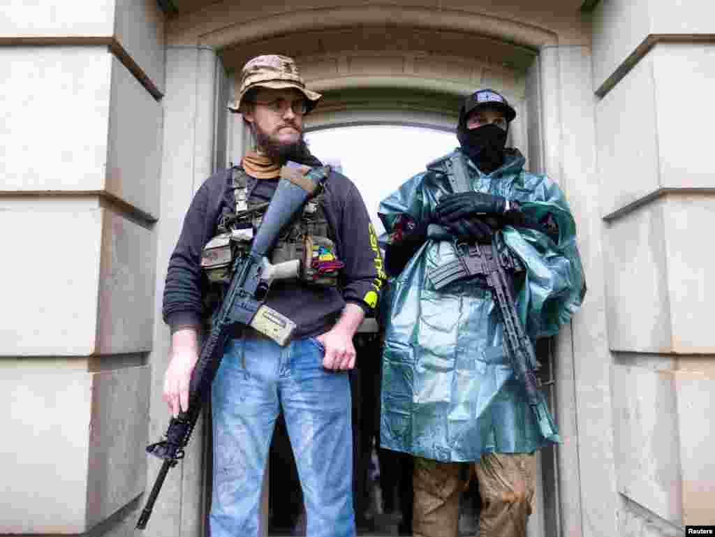 Protesters with long guns shelter from the heavy rain during a protest against Governor Gretchen Whitmer&#39;s extended stay-at-home orders to slow the spread of the coronavirus disease (COVID-19), at the Capitol building in Lansing, Michigan.