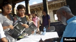FILE - Cuban author Leonardo Padura autographs his book "The Faces of Padura" in Havana, Oct. 31, 2015. Previously, Padura was awarded the 2015 Princess of Asturias award for literature.
