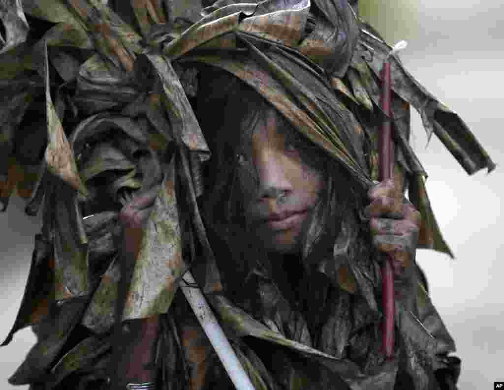 A muddied girl, donning a cape made of dried banana leaves, collects candles before attending a mass to celebrate the Feast Day of St. John the Baptist in the village of Bibiclat, Aliaga township, Nueva Ecija province in northern Philippines.