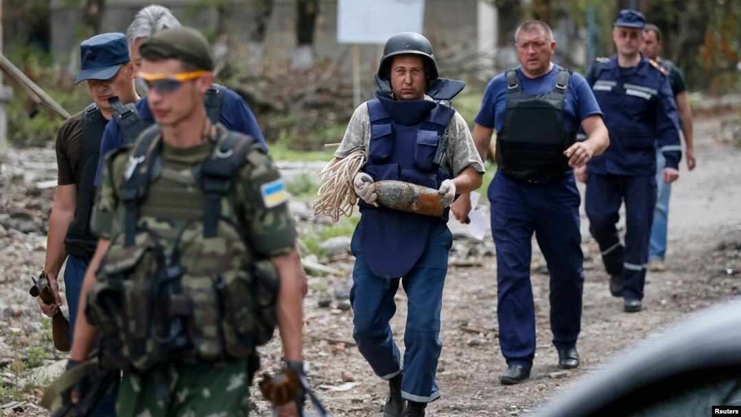 A sapper, center, carries a deactivated 120mm mortar shell after a defusing operation in the village of Semenovka, eastern Ukraine, July 13, 2014. 