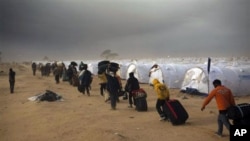 Men, who used to work in Libya and fled the unrest in the country, carry their belongings as they arrive during a sand storm in a refugee camp at the Tunisia-Libyan border, in Ras Ajdir, Tunisia, March 15, 2011