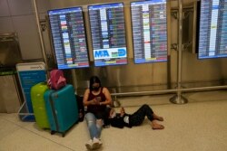 Seorang perempuan dan anak-anak dari Brazil menunggu penerbangan mereka di bawah papan yang menunjukkan banyak penerbangan yang dibatalkan, di Bandara Internasional Miami, Senin, 27 Desember 2021. (Foto: AP)