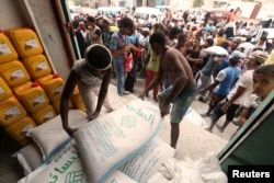 FILE - Workers unload sacks of wheat flour as people gather outside an aid distribution center in the Red Sea port city of Hodeida, Yemen, June 14, 2018.