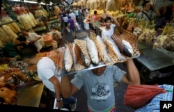 A vendor carries cooked fish for sale at a Chinese market during the upcoming Chinese New Year celebrations in Bangkok, Thailand, Wednesday, Feb. 14, 2018. Chinese New Year falls on Feb. 16 this year, marking the start of the Year of the Dog. (AP Photo/Sa