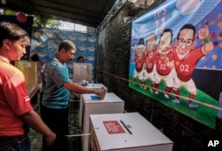 Voters cast their ballot as caricatures of presidential candidates and their running mates is are seen on the wall at a polling station in Yogyakarta, Indonesia, April 17, 2019.